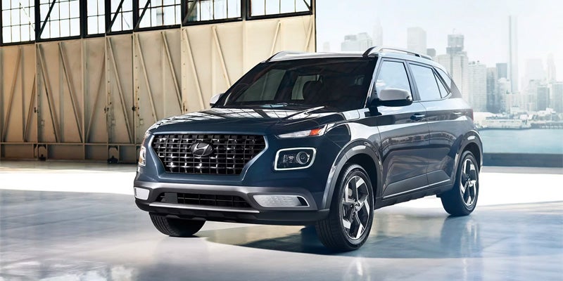 A blue Hyundai Venue parked indoors, with a city skyline and water visible in the background.