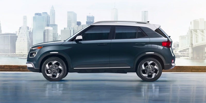 A Hyundai Venue SUV with a white roof is parked with a city skyline in the background.