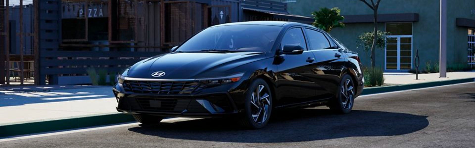 A shiny black Hyundai Elantra is parked directly in front of an urban building, facing the left.