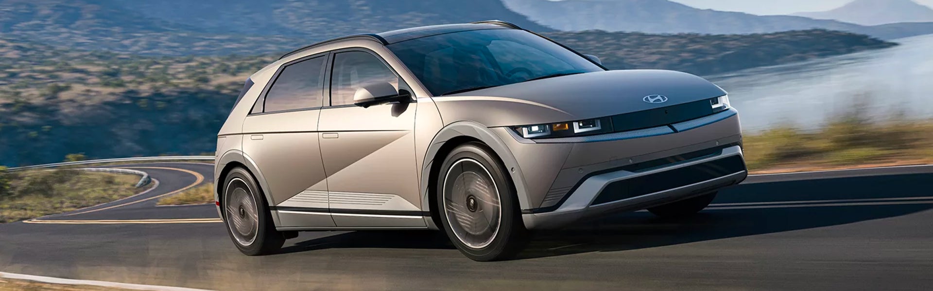 Hyundai IONIQ 5 drives on a winding road with mountains and water in the background.