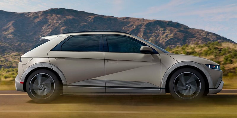 Side profile of Hyundai IONIQ 5 driving on an open road with mountains in the background.