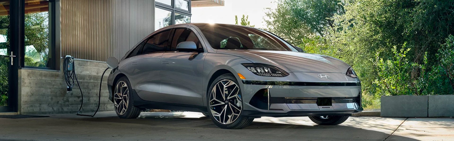 A silver Hyundai electric car is charging in front of a modern building with a wall of green foliage.