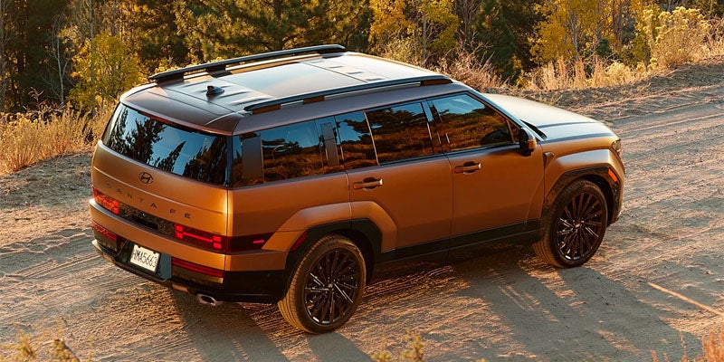 Bronze Hyundai Santa Fe SUV on a dirt road, viewed from the rear passenger side.