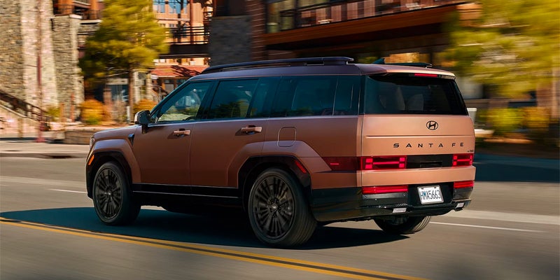 Rear view of a Hyundai Santa Fe SUV driving on a road, with buildings and trees in the background.
