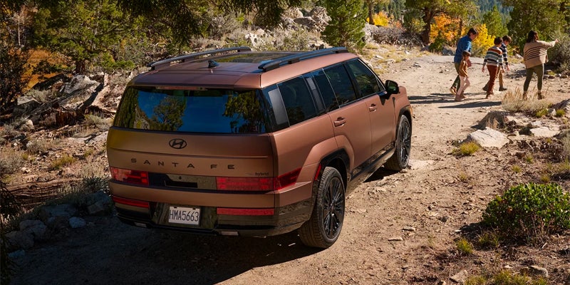 A Hyundai Santa Fe SUV on a dirt road, with three people walking right in the background.