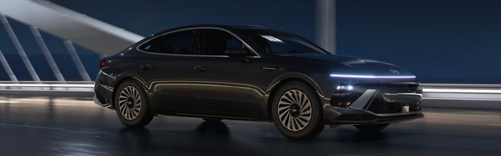 A sleek, Hyundai Sonata car drives on a road with light reflecting off its side.