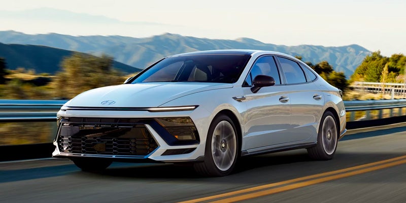 A white Hyundai Sonata sedan driving on a mountain road.