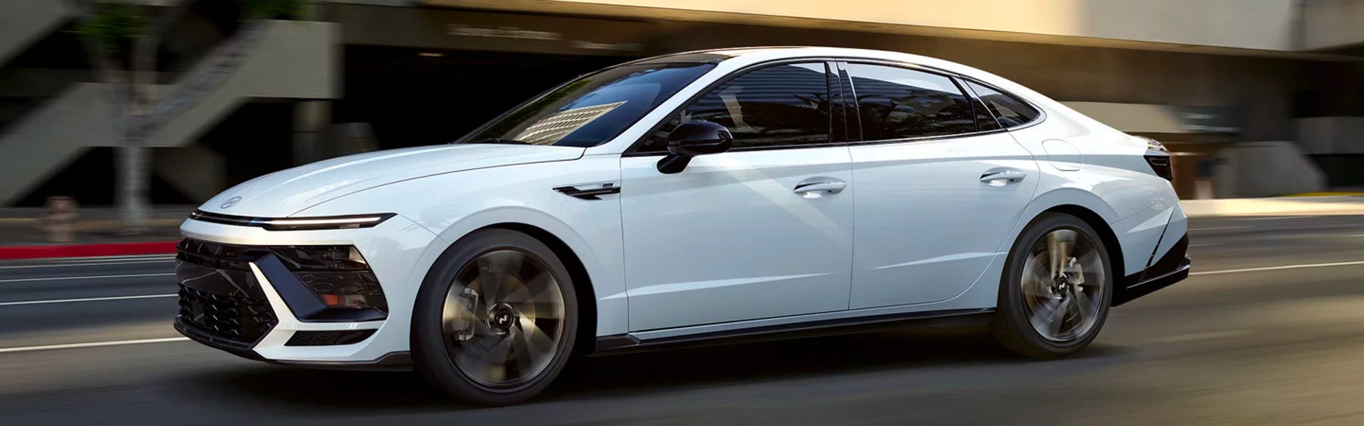 A Hyundai Sonata Hybrid sedan with a black roof and black trim, speeding on a multi-lane roadway with buildings in the background.