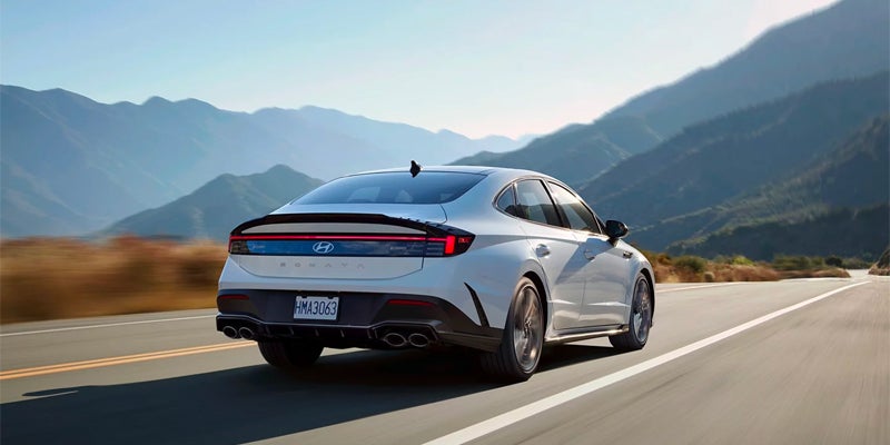 Rear view of a Hyundai Sonata Hybrid car driving on a scenic highway with mountains in the background.