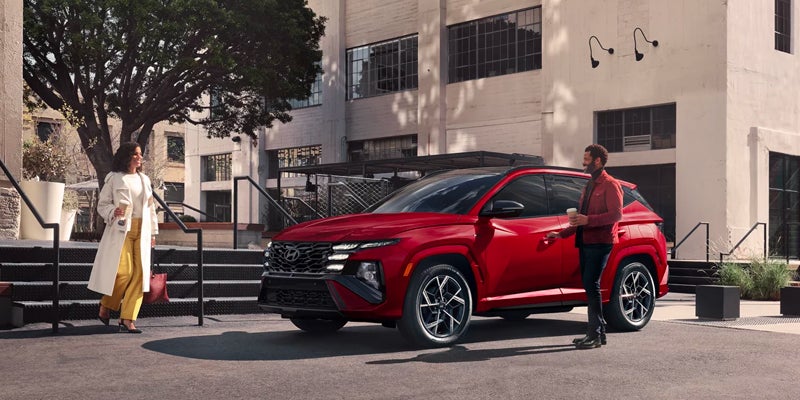 A Hyundai Tucson Hybrid parked on a paved area with a man standing by its door and a woman walking towards it.