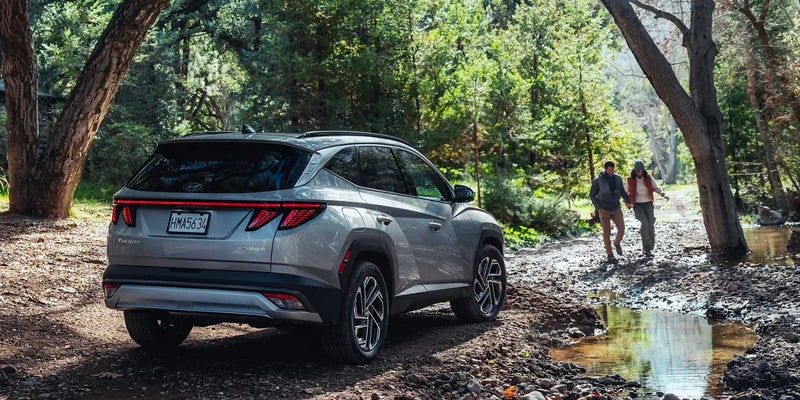 Hyundai Tucson Plug-In Hybrid parked on a dirt path in the woods, with two people walking away from it into the trees.