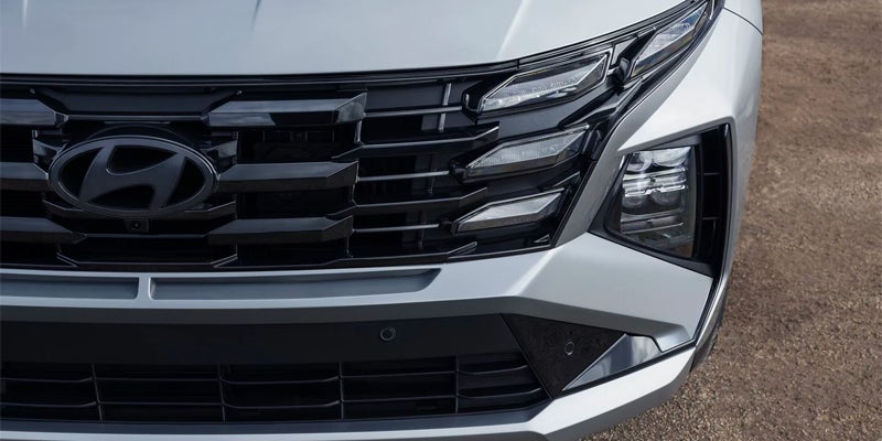 Close-up of a Hyundai Tucson Plug-In Hybrid car's front grille, headlight, and bumper.